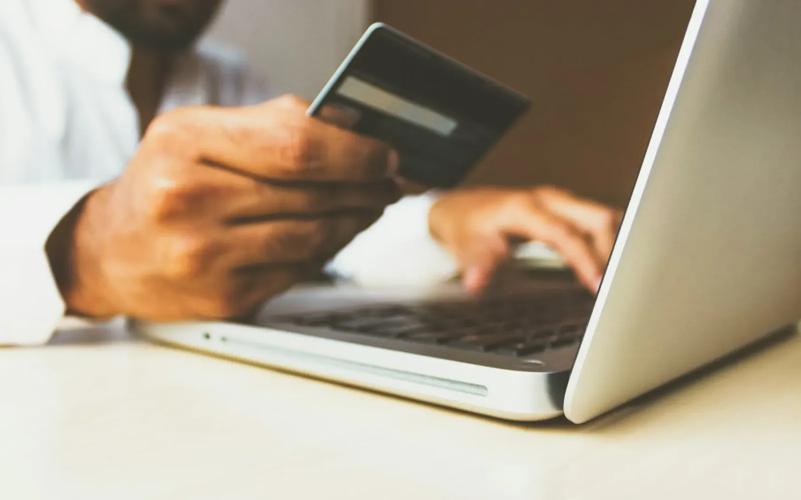 A person shopping online on a laptop while holding a payment card